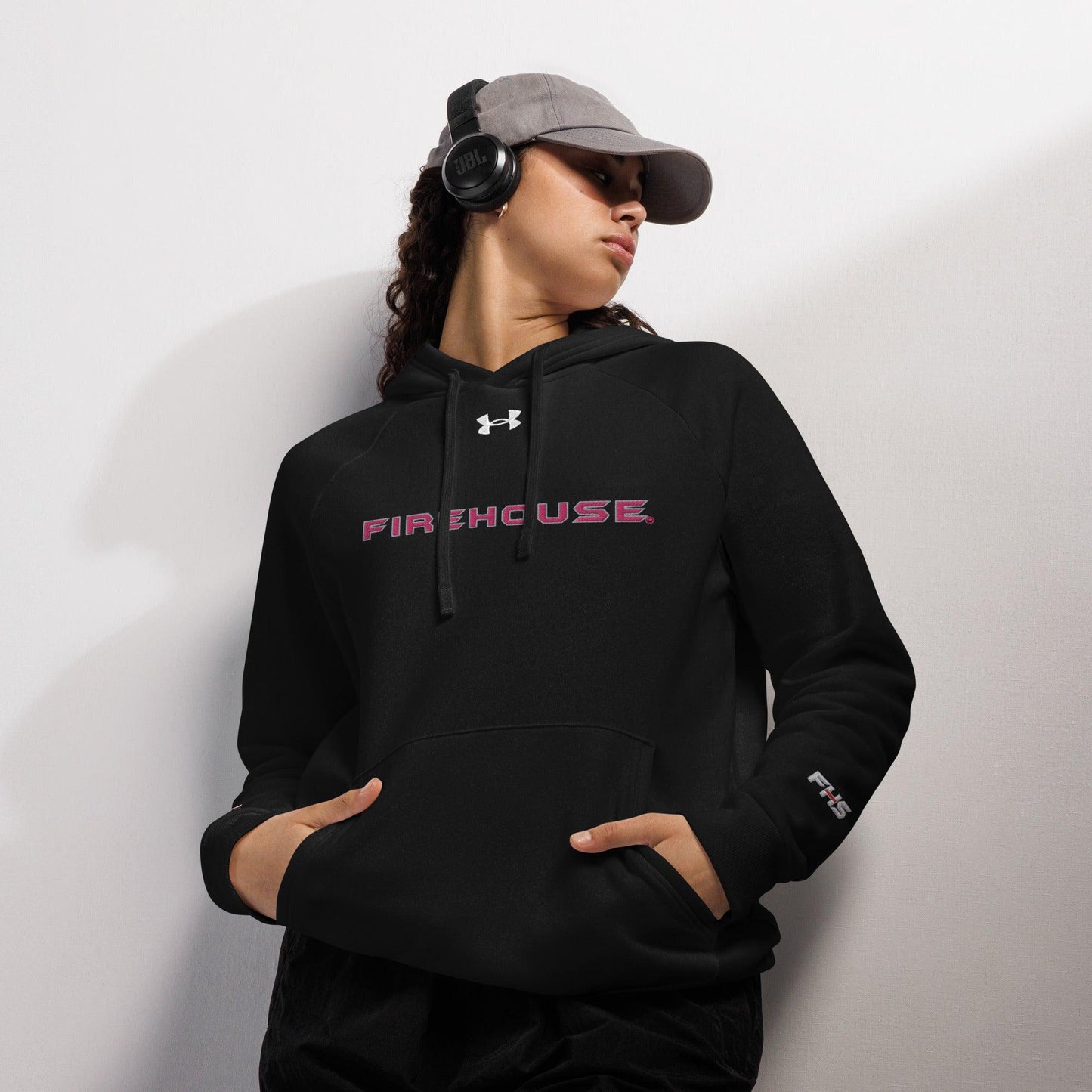 Black Under Armour® Firehouse pullover hoodie, perfect firefighter apparel for style and comfort, worn by a model with headphones.